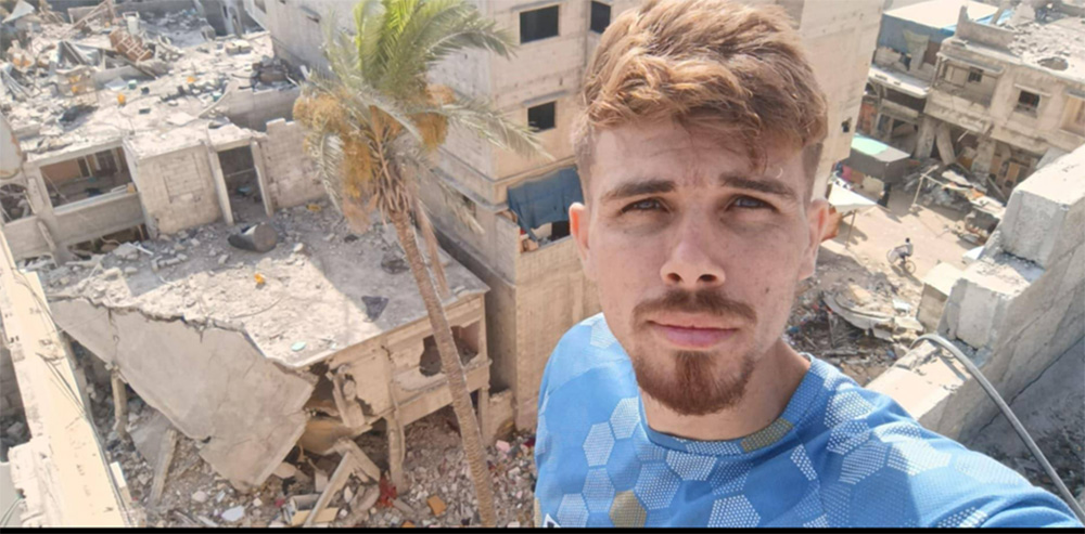 Mahmoud taking a selfie overlooking a destroyed apartment building in Gaza